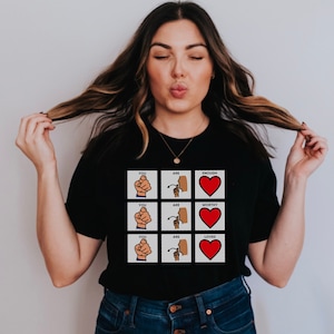 Puede incluir: Una camiseta negra con un gráfico de tres señales de mano y corazones. Las señales dicen "Eres suficiente", "Eres digno", y "Eres amado".