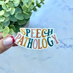 Puede incluir: Una pegatina con el texto "SPEECH PATHOLOGY" en un arcoíris de colores, incluyendo azul verdoso, naranja, rosa y amarillo.