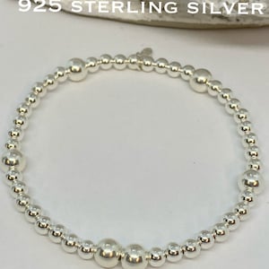 May include: A silver beaded bracelet with a larger bead in the centre. The bracelet is made of 925 sterling silver and has the text "Bella" on the bottom of the image.
