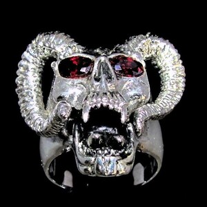 Può includere: Un anello d'argento con un designo di teschio dettagliato, con due corna e occhi di pietre preziose rosse.