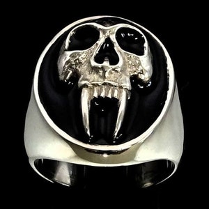 May include: A silver ring with a black enamel background featuring a detailed skull with large fangs.