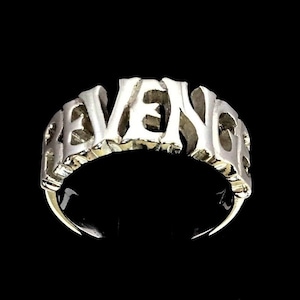 May include: A silver ring with the word "REVENGE" spelled out in bold, raised letters.