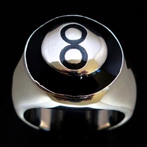 May include: A silver-toned ring featuring a black and white eight ball design. The ring has a polished finish and a wide band. The number eight is prominently displayed in the center of the ball, set against a black background.