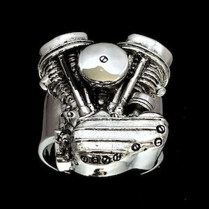Puede incluir: Un anillo de plata con un diseño detallado de motor de motocicleta. El anillo está hecho de plata de ley y presenta una representación realista de un motor bicilíndrico en V.