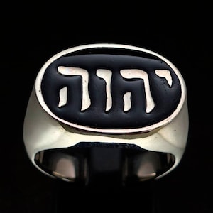 May include: A silver ring with a black oval inlay featuring the Hebrew word "Chai" in white lettering.