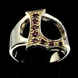 May include: A silver ring with a gold letter 'L' set with red gemstones. The ring is designed with a thick band and a bold, stylized letter.