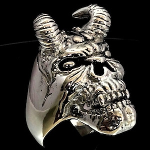 Può includere: Un anello d'argento con un designo di teschio dettagliato con corna. Il teschio ha un'espressione minacciosa con denti affilati e orbite profonde.