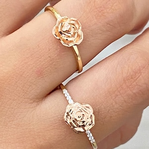 May include: Two gold rose rings. The ring on the top has a plain band. The ring on the bottom has a band with small clear stones.