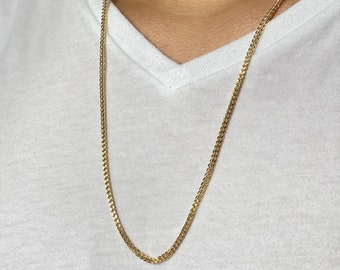 May include: A gold chain necklace with a delicate, intricate design. The chain is worn by a person with a white shirt.