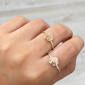 Pu&ograve; includere: Due anelli d'oro con disegni di rose. L'anello superiore ha un design di rosa semplice, mentre l'anello inferiore ha un design di rosa con piccoli pietre chiare intorno al bordo.