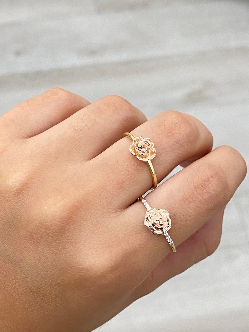 Pu&ograve; includere: Due anelli d'oro con disegni di rose. L'anello superiore ha un design di rosa semplice, mentre l'anello inferiore ha un design di rosa con piccoli pietre chiare intorno al bordo.