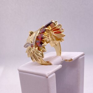 May include: A gold ring with a detailed design of a lion's head with red and white gemstones. The ring is marked "14K" on the band.