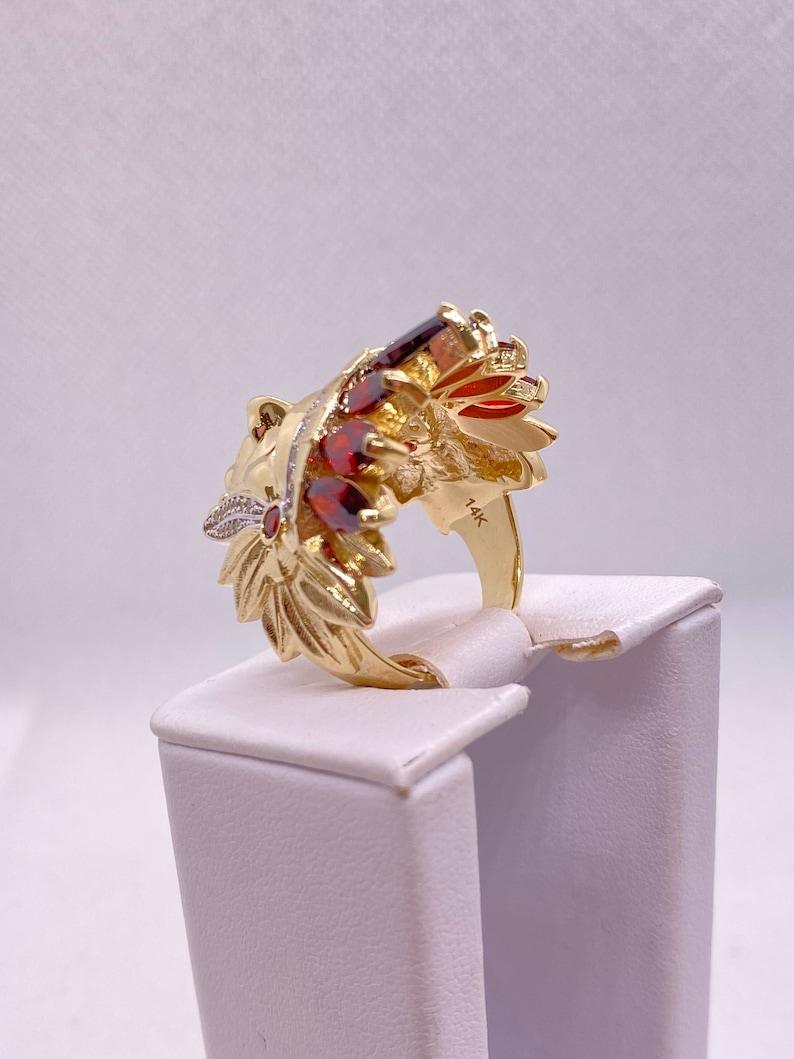 May include: A gold ring with a detailed design of a lion's head with red and white gemstones. The ring is marked "14K" on the band.