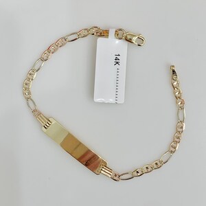 May include: A gold bracelet featuring an ID plate and a chain link design. The bracelet has a rectangular plate in the centre and a clasp closure. A white tag with the text "14K" is attached to the bracelet.