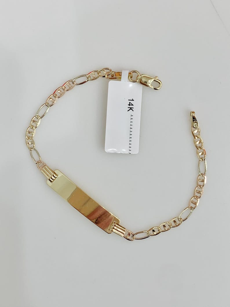May include: A gold bracelet featuring an ID plate and a chain link design. The bracelet has a rectangular plate in the centre and a clasp closure. A white tag with the text "14K" is attached to the bracelet.