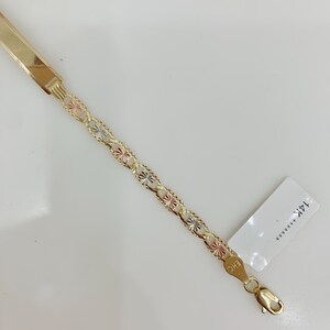 May include: A gold bracelet with a flat bar and a chain of star-shaped links in gold, rose, and white gold. The bracelet has a lobster clasp and a tag with text.