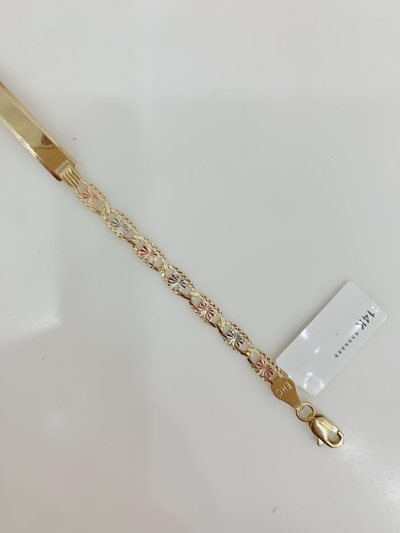 May include: A gold bracelet with a flat bar and a chain of star-shaped links in gold, rose, and white gold. The bracelet has a lobster clasp and a tag with text.