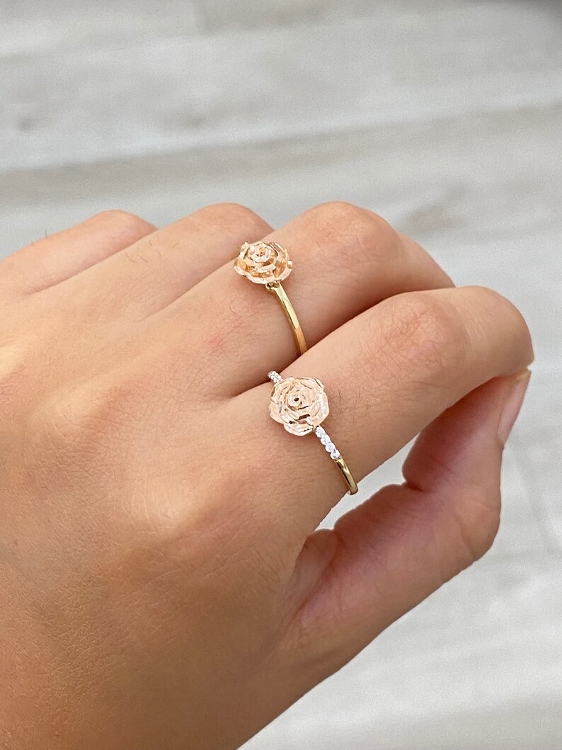 Pu&ograve; includere: Due anelli d'oro a forma di rosa. Un anello ha un design semplice a forma di rosa, mentre l'altro ha un design a forma di rosa con piccoli pietre intorno alla fascia.