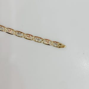 May include: A gold-colored bracelet with an oval link chain design. Each link features a starburst pattern. The bracelet is shown against a white background.
