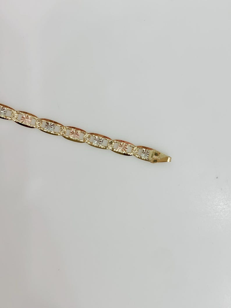 May include: A gold-colored bracelet with an oval link chain design. Each link features a starburst pattern. The bracelet is shown against a white background.