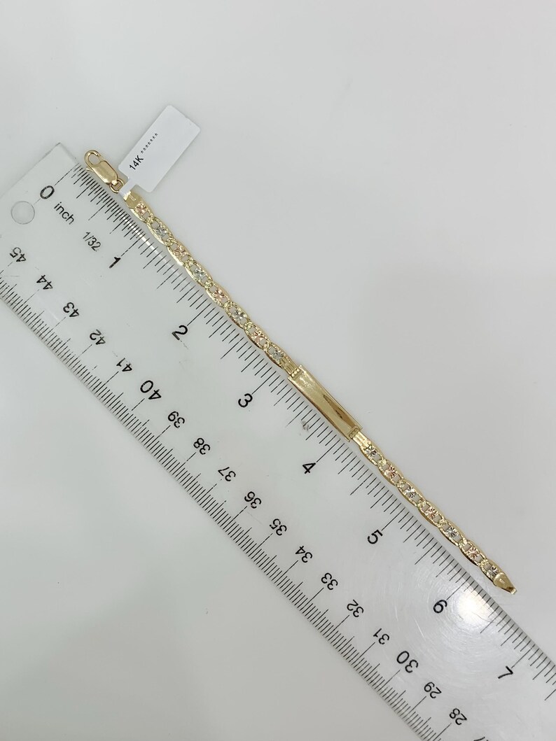 May include: A gold-colored bracelet with a rectangular bar and a line of small, clear stones. The bracelet is measured with a ruler, showing a length of approximately 6 inches. A tag with "14K" is attached.