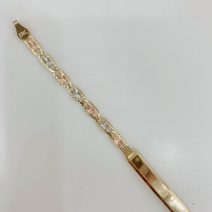May include: Gold-toned bracelet with a rectangular nameplate and a chain of alternating gold, rose gold, and silver-toned starburst links. The bracelet has the letters "ERC" stamped on the clasp.