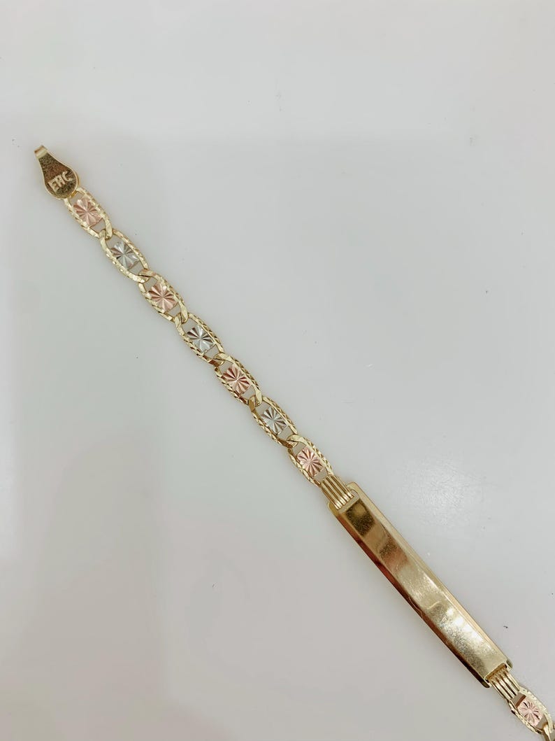 May include: Gold-toned bracelet with a rectangular nameplate and a chain of alternating gold, rose gold, and silver-toned starburst links. The bracelet has the letters "ERC" stamped on the clasp.