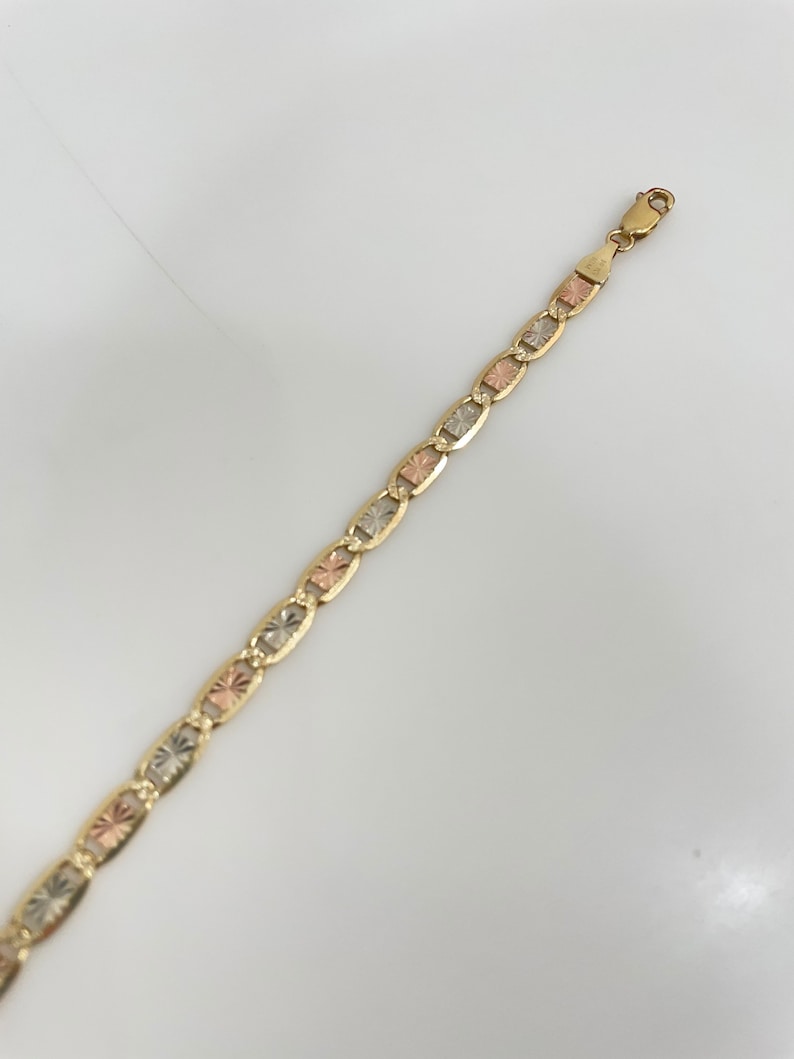 May include: A gold chain bracelet with a tri-color design. The chain is made of interlocking oval links with a textured surface.