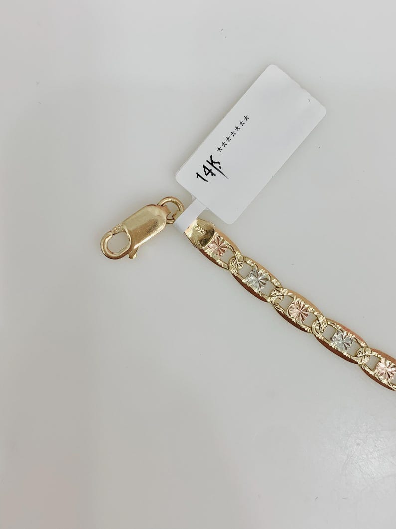 May include: A gold-colored chain bracelet with a lobster clasp. The chain links feature a starburst design with alternating gold, silver, and rose gold tones. A white tag with "14K" is attached.