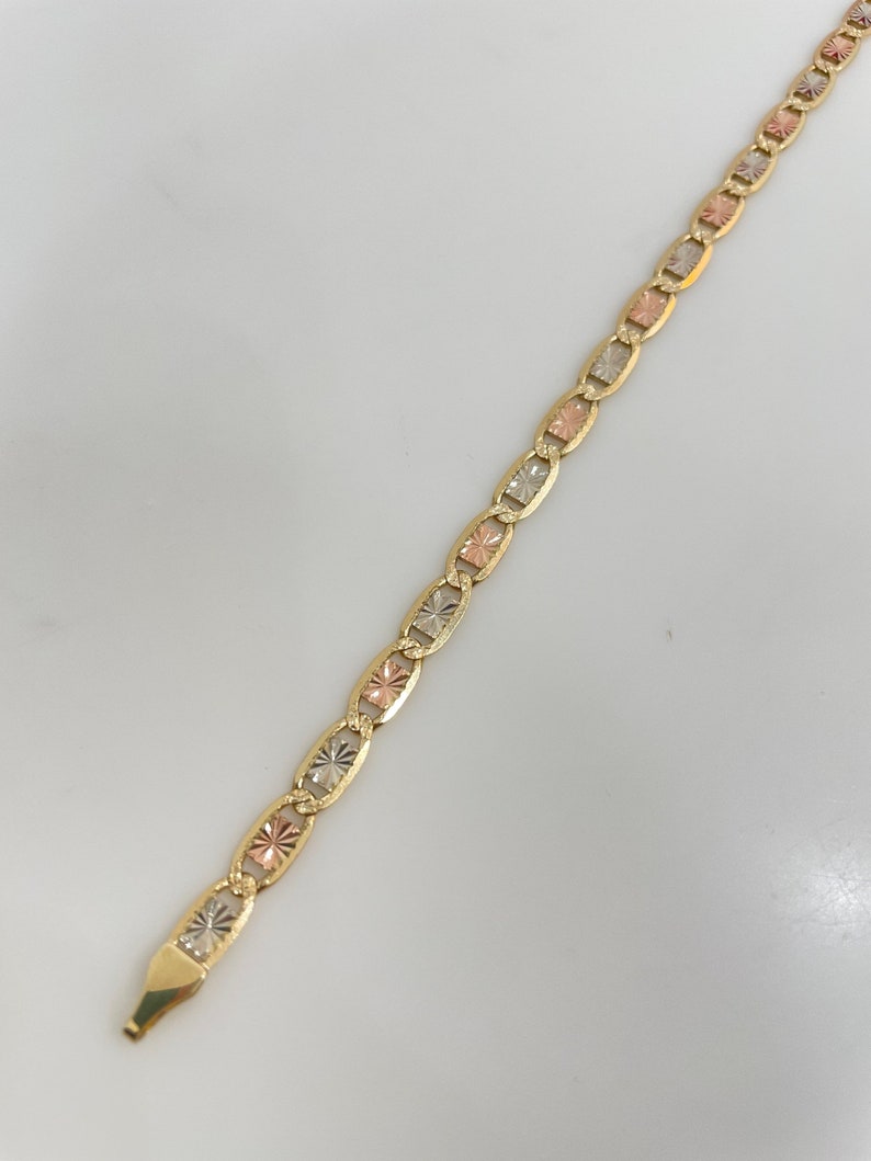 May include: A gold chain bracelet with a mariner link design. The chain is made of three different colors of gold: yellow, white, and rose.