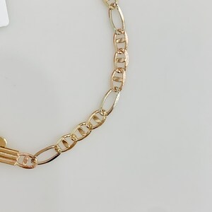 May include: A gold-coloured chain necklace featuring a combination of oval and rounded links. The chain has a bright, polished finish, reflecting light. The design is simple and elegant, suitable for everyday wear. The necklace is shown against a plain white background.