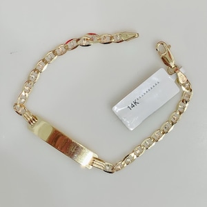May include: A gold-colored bracelet with a rectangular nameplate and a chain link design. The bracelet has a lobster clasp closure and a small tag that reads "14K". The bracelet is displayed on a white surface.