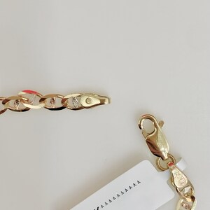 May include: A gold-colored chain necklace with a lobster clasp and a tag that reads "14K". The chain links are a curb style, with alternating smooth and textured sections. The jewelry is displayed against a white background.