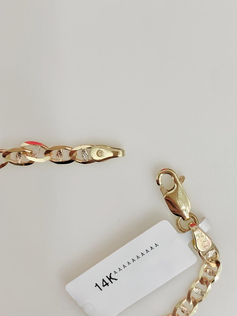 May include: A gold-colored chain necklace with a lobster clasp and a tag that reads "14K". The chain links are a curb style, with alternating smooth and textured sections. The jewelry is displayed against a white background.