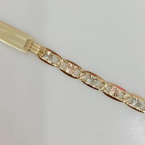 May include: A gold-toned bracelet with a decorative chain design. The chain links alternate between a smooth, oval shape and a square, starburst pattern. The clasp is a simple, rectangular design.