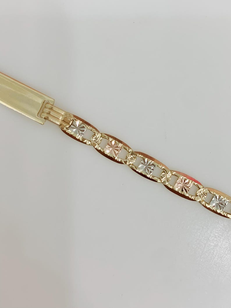 May include: A gold-toned bracelet with a decorative chain design. The chain links alternate between a smooth, oval shape and a square, starburst pattern. The clasp is a simple, rectangular design.