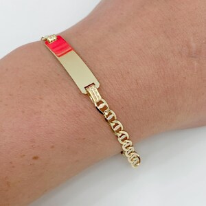 May include: A gold-colored bracelet with a rectangular nameplate and a chain link design. The nameplate is smooth and polished, and the chain links are small and connected. The bracelet is worn on a wrist.
