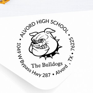 May include: A black and white round return address stamp with the text "Alvord High School", "The Bulldogs", "1049 W Bypass Hwy 287", "Alvord, TX 76225". The stamp features a cartoon bulldog with a spiked collar.