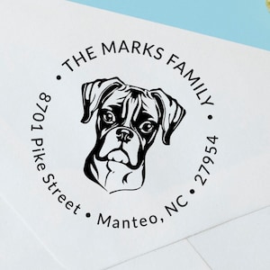 May include: A round return address stamp with a black and white illustration of a boxer dog. The text reads "The Marks Family, 8701 Pike Street, Manteo, NC 27954."