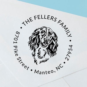 May include: A round return address stamp with a black and white illustration of a dog's head. The text reads "The Fellers Family", "8701 Pike Street", "Manteo, NC", and "27954".
