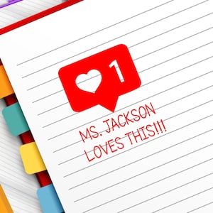 May include: A spiral-bound notebook with lined pages and a red cover. A red speech bubble with a heart and the number 1 is on the page. The text "MS. JACKSON LOVES THIS!!!" is also on the page. A yellow pencil, paper clips, and other stationery items are in the image.