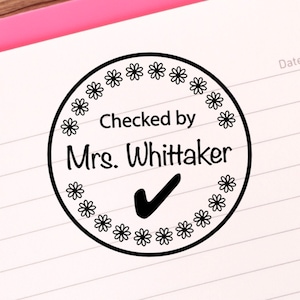 May include: Black and white teacher stamp with a circle border of small flowers. The stamp says "Checked by Mrs. Whittaker" with a checkmark.