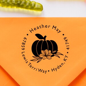 May include: A black and white return address stamp with a pumpkin and flower design. The text reads "Heather May", "67859 Lewis Terri Way", "Hyden, KY 41749".