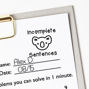 May include: A white sheet of paper with the words "Incomplete Sentences" and a koala bear illustration. The name "Alex D." and the date "08/15" are written on the sheet. A gold-colored clip holds the paper to a gray clipboard.