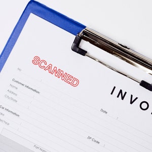 May include: A white clipboard with a blue top and a silver clip. The clipboard has a form with the word "SCANNED" in red letters and the word "INVO" at the bottom right corner.