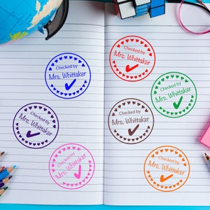 May include: Six colorful round teacher stamps with a checkmark and the text "Checked by Mrs. Whittaker" in a circle of hearts.