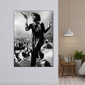 Puede incluir: Fotografía en blanco y negro de un músico actuando en un escenario frente a una gran multitud. El músico lleva una camisa con estampado en blanco y negro y una bufanda. La multitud aplaude y agita las manos en el aire.