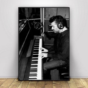 May include: A black and white photo of a person playing a piano with headphones on. The person is wearing a dark shirt and jeans. The piano is a grand piano with a black finish.