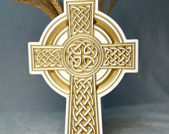 May include: A white and gold Celtic cross with intricate knotwork designs. The cross features a circular center and detailed patterns throughout, with a gold border. The background includes wheat stalks.