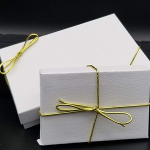 May include: Two white gift boxes with gold ribbon tied in bows. The boxes are on a black surface.